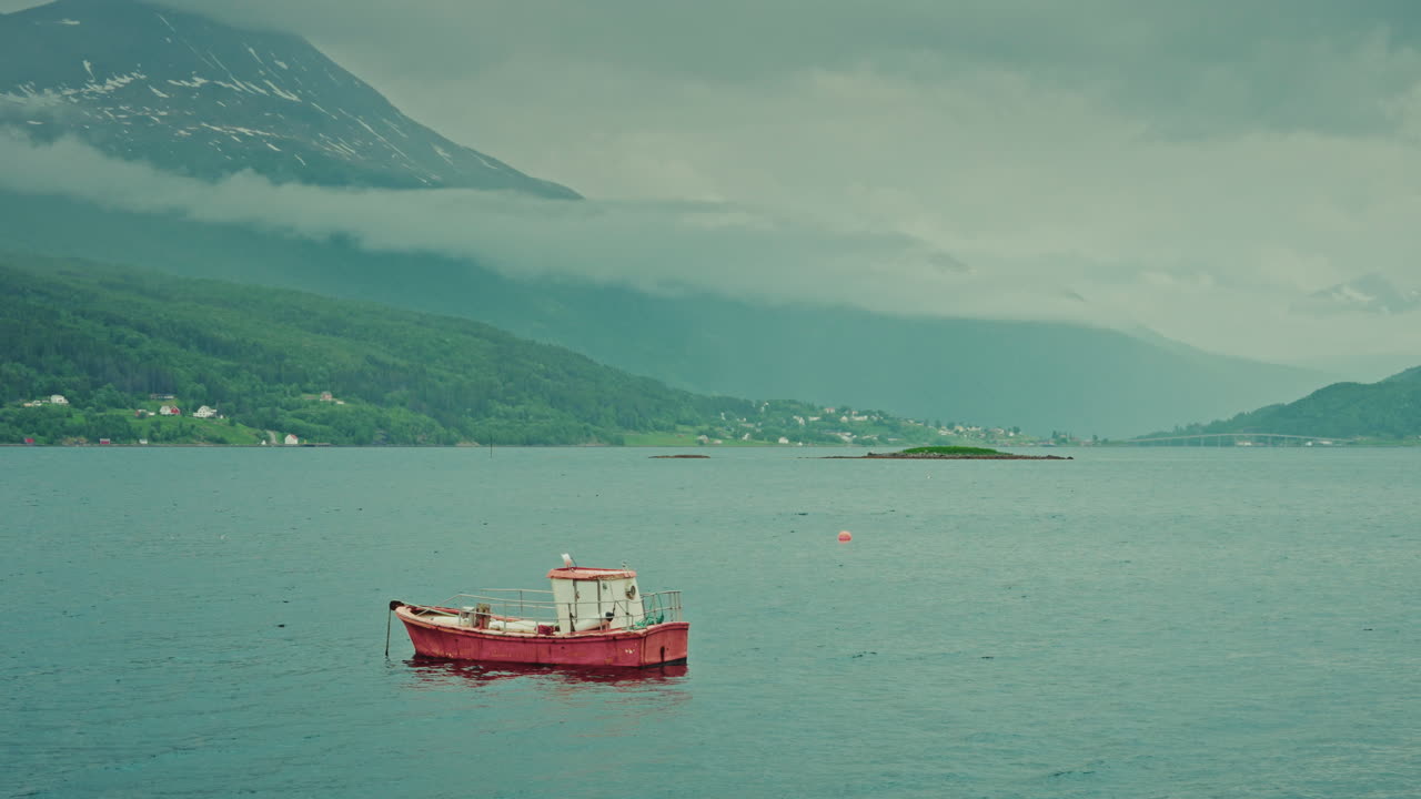 Close up static shot of an old small fishing boat anchored in the sea in Norway. View of the cold weather nordic landscape.