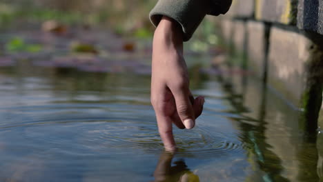 close up woman hand splashing water enjoying touching fresh pond in nature park outdoors