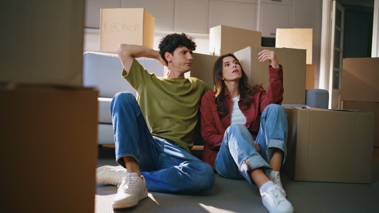 Tired couple moving house sitting floor modern living room between carton boxes