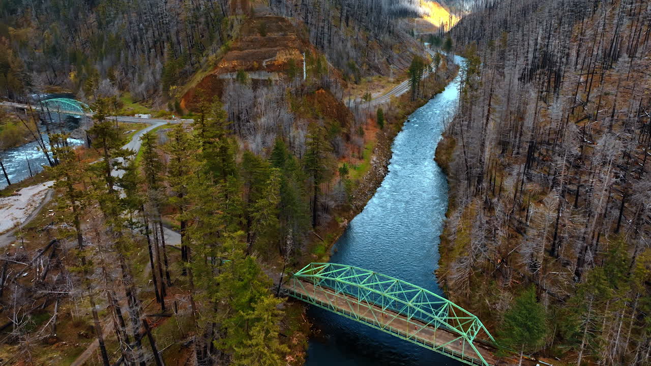 Approaching the little metal bridge over the narrow quick mountain river. Dead dry forest cover the rocks. Top view.