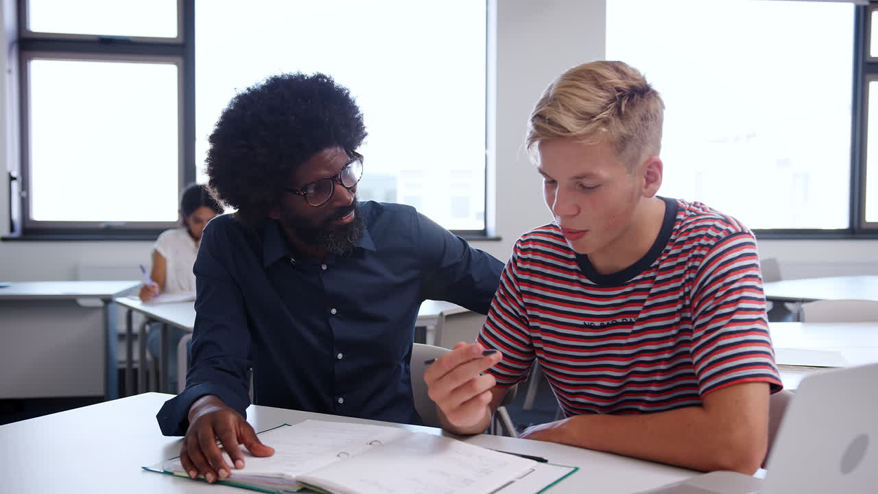 tutor de la escuela secundaria dando a los estudiantes varones una a una matrícula en el escritorio en el aula