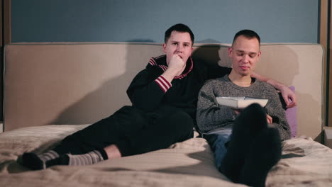 two men relaxing and eating on bed