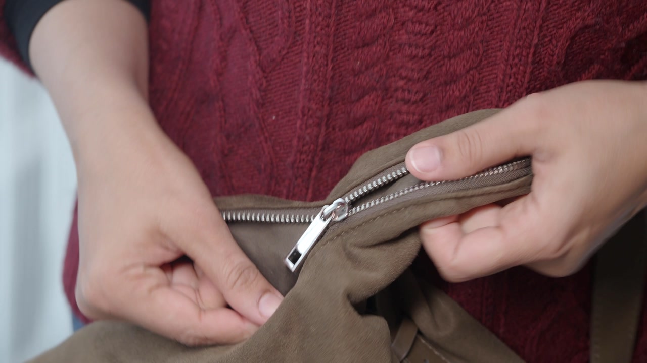 Close-Up of Hands Fixing a Broken Zipper on a Brown Bag
