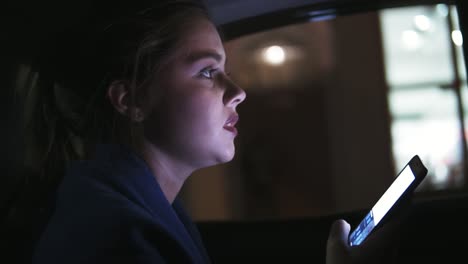 beautiful girl riding in a taxi at night sitting on the backseat and holding her phone. she is worried, trying to find something