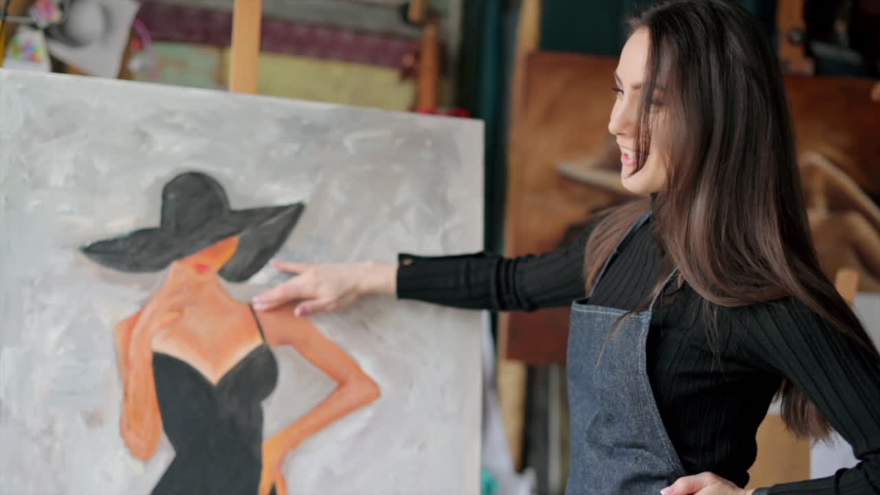 Woman painter wearing black clothes painting woman model face with hat drawing with red brush at a workshop