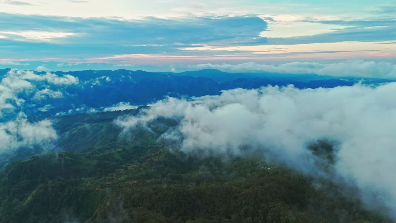 Cinematic drone aerial of rolling clouds sweeping across layered green mountain ridges at dawn. Ideal for travel, nature, mindfulness, and environmental storytelling