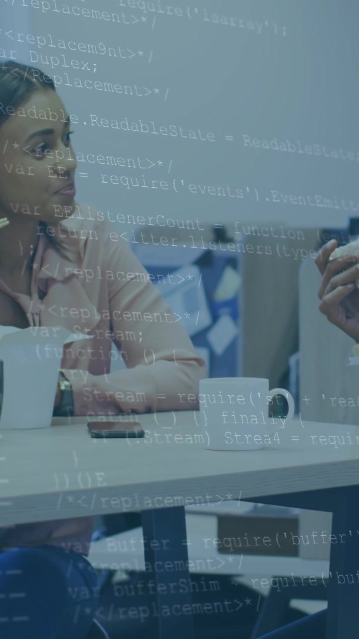 Vertikal video: Kvinde læner sig og nikker under arbejde, efter en kollega har gestikuleret, mens kode overlejrer telefonen.