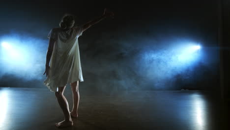 Modern-dance-girl-in-a-white-dress-dances-a-modern-ballet-jumps-on-the-stage-with-smoke-in-the-blue-spotlights.