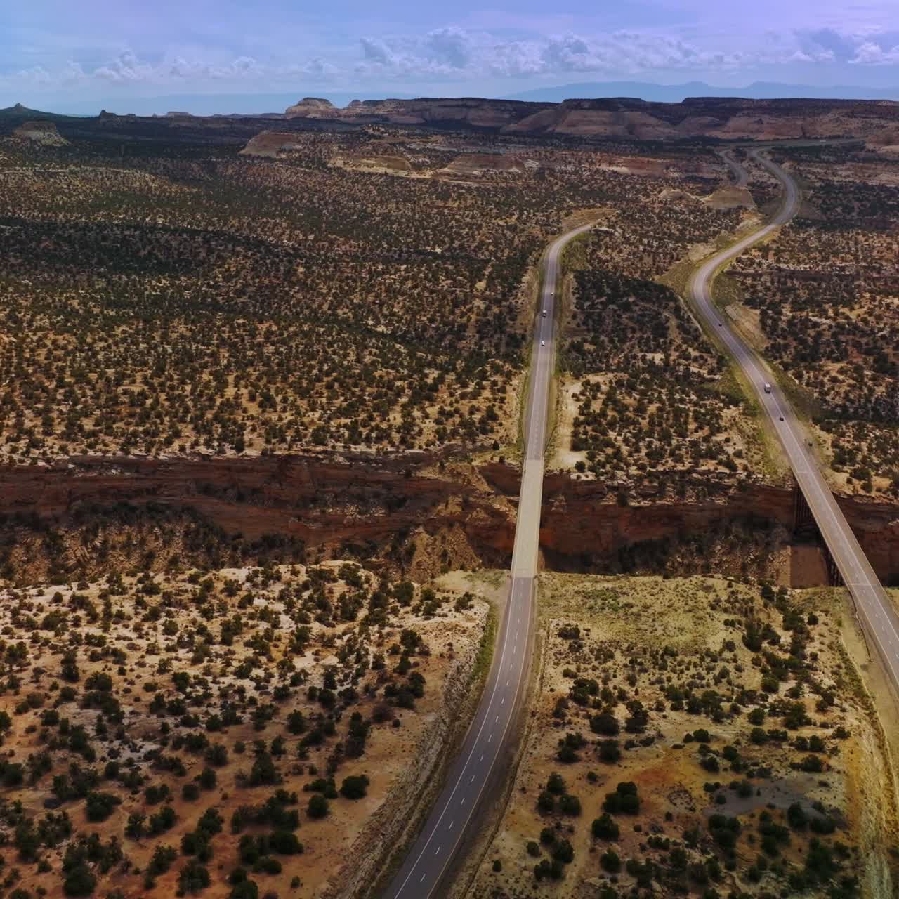 Two long highways passing through the deserted land with little green bushes. Drone approaching the huge crack in the desert with bridges connecting the roads