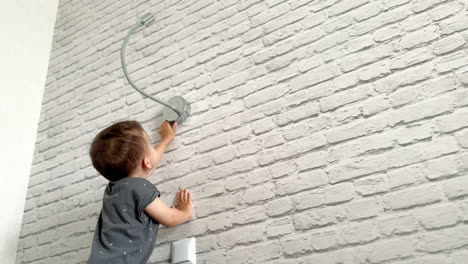 lovely caucasian toddler standing near the wall looks back. kid turns to the lamp to switch it on and off. low angle view.