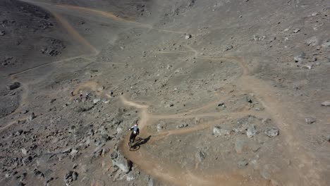 el dron sigue y orbita alrededor de un ciclista de montaña cuesta abajo mientras ve gira en una esquina afilada en senderos de tierra por una ladera rocosa