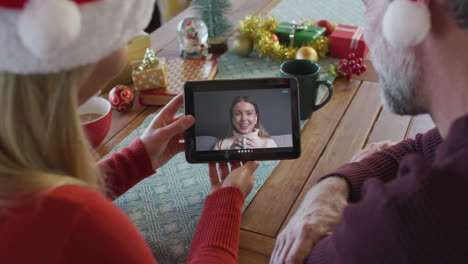 Caucasian-couple-with-santa-hats-using-tablet-for-christmas-video-call-with-woman-on-screen