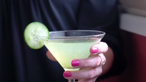 cucumber martini slowly picked up from table and carried out of frame by woman’s hands closeup with pink nail polish