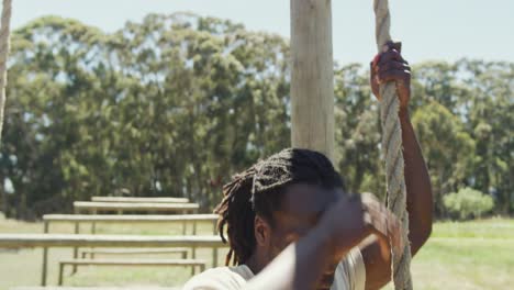 fit african american male soldier with deadlocks climbing down rope on army obstacle course