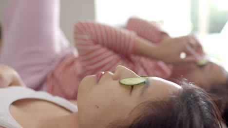 relaxing at home, diverse women friends lying down with cucumber slices on eyes