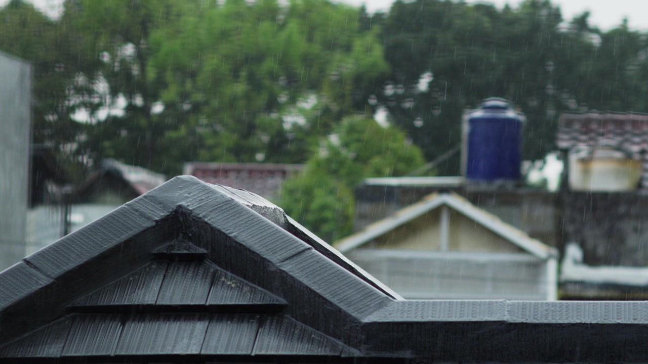 Tropical monsoon rain pours over clay roof tiles in Jakarta. Intermittent lightning flashes illuminate the stormy sky. High-intensity weather footage captured in Indonesia