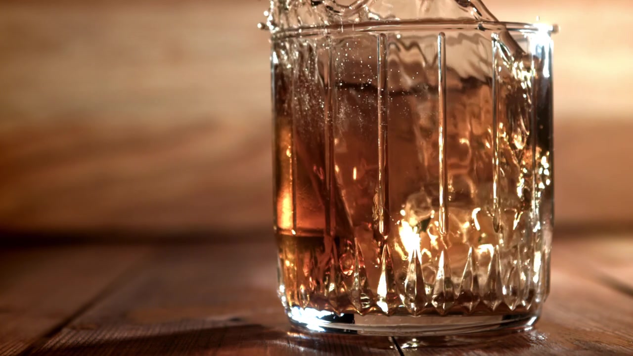 Cubetto di ghiaccio che schizza al rallentatore in un bicchiere di whisky.