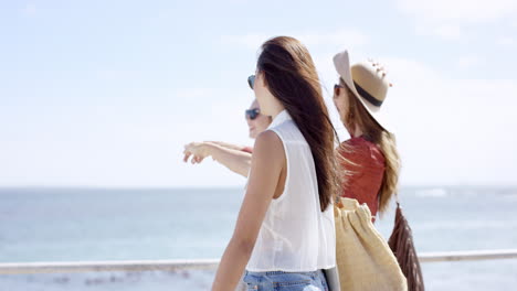 Three-young-women-tourists-on-summer-vacation-walking-on-beach-promenade