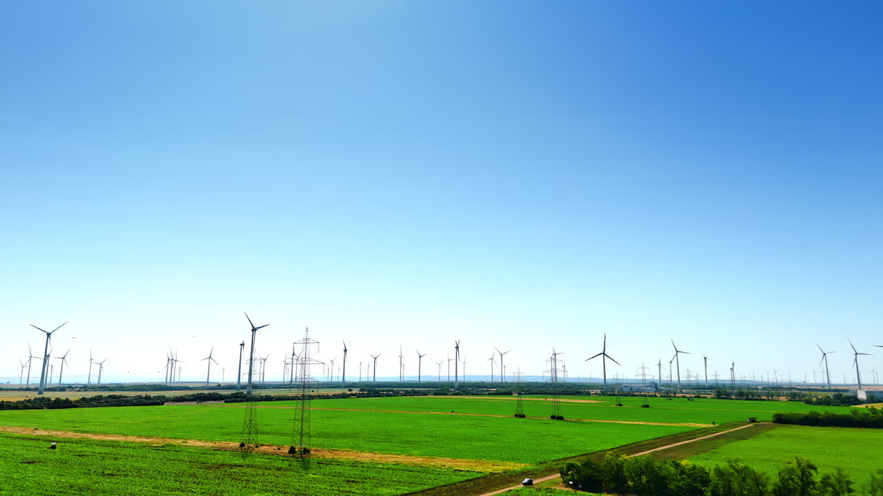 Turbines produce clean energy. Expansive green fields host numerous wind turbines under a clear blue sky, producing renewable energy