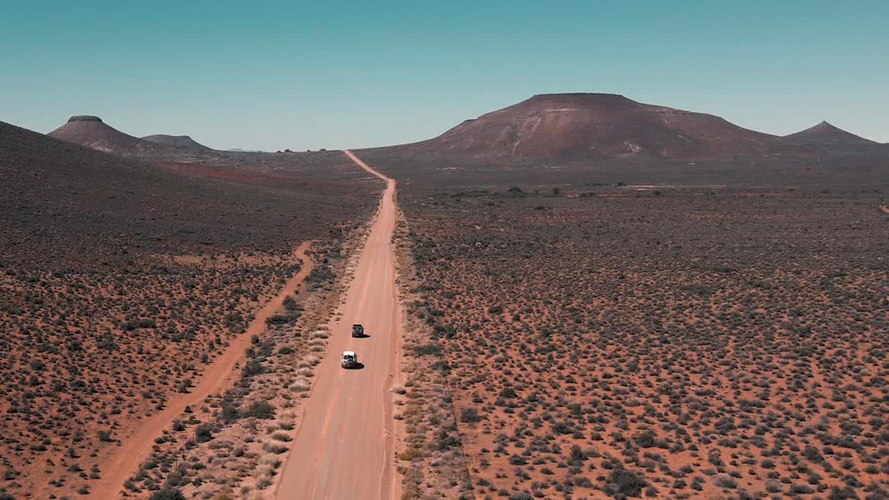 Two cars drive on a vast dirt road in the Karoo of South Africa