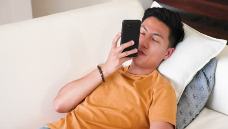 relaxing on couch, young man browsing smartphone at home, enjoying leisure time