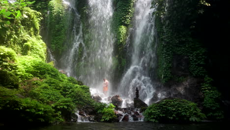 guy takes refreshing shower under impressive bali waterfall in lush jungle