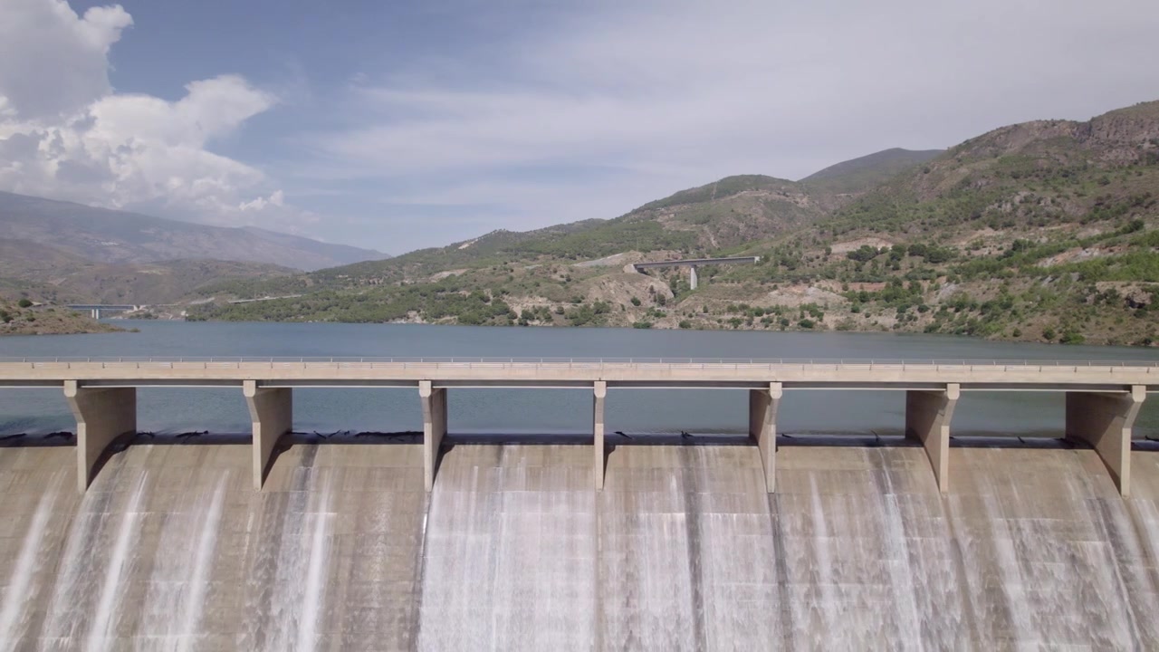 Dam spillway releasing water. Travel aerial view. Reservoir full operations. Water discharge from the upper section of a gravity dam. Rules Dam. Spain.