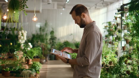 man browsing plants on tablet in a green plant nursery