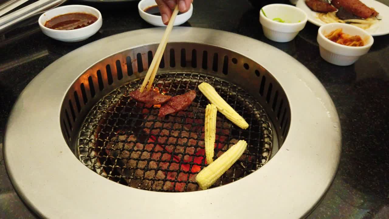 mazorcas de maíz, un trozo de carne quemada, salchichas en rodajas, dos pares de palillos que se mueven y toman la comida en su plato, sentí hambre mientras escribía esto