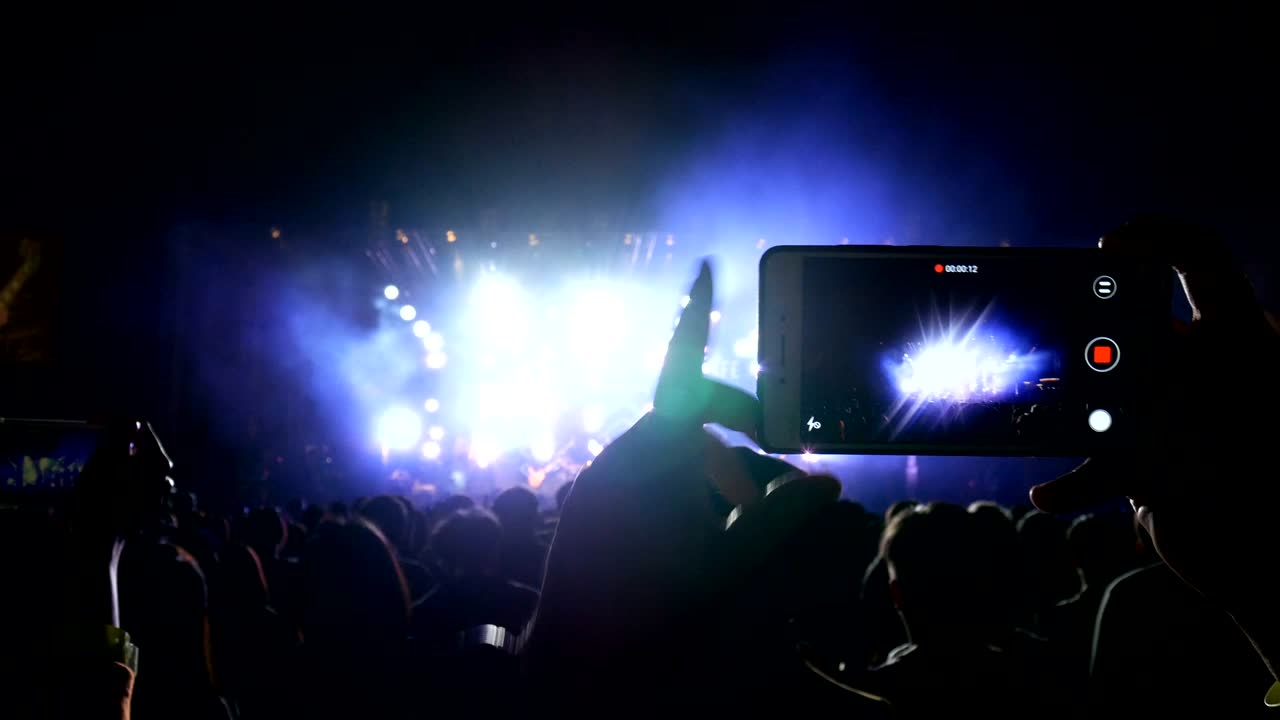 스마트 폰을 들고 있는 사람들이 춤추는 음악 페스티벌의 비디오 그룹을 녹음하고 있습니다.