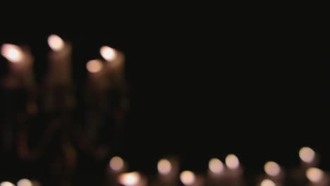 a group of white candles some on a candelabra lit up out of focus and pulled into focus in slow motion