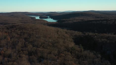 Slow-drone-spin-looking-far-into-the-distance-over-forested-hills-with-a-gorgeous-lake-in-the-distance-at-winter-sunrise