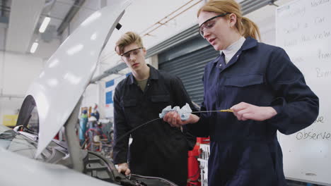 estudiantes masculinos y femeninos comprobando el nivel de aceite del coche en el curso de aprendizaje de mecánico de automóviles en la universidad