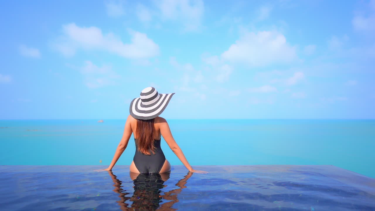 Eine gesunde, fitte Frau sitzt am Rand eines Infinity-Pools mit Blick auf den Meereshorizont.