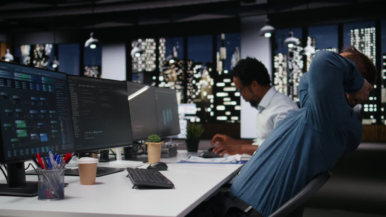 Man Working on Multiple Computer Screens in Modern Office at Night