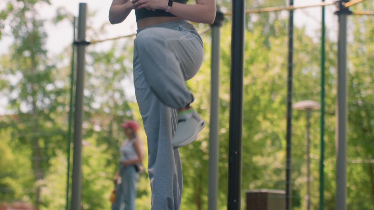 Close up of young woman performing leg exercises in outdoor park setting wearing gray sweatpants and white sneakers. focus remains on her lower body as woman lifts one knee at time
