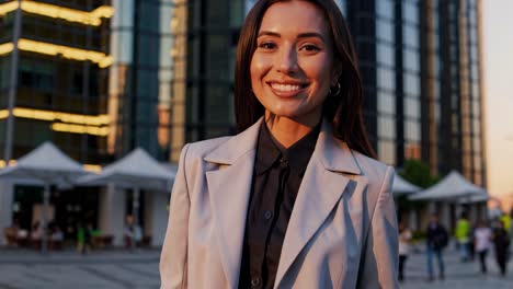 professional businesswoman standing confidently against modern city architectural backdrop, radiating success and career driven energy during golden hour lighting