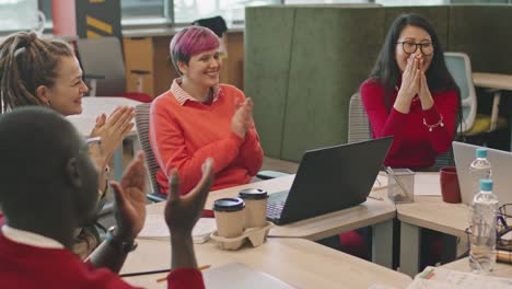 group of workers sitting at a table and clapping in a meeting