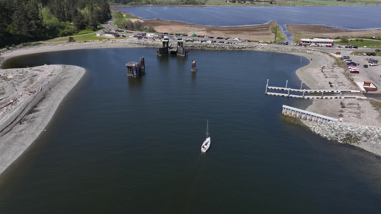 Wide drone shot of a sailboat sailing into Whidbey Island's boat launch.