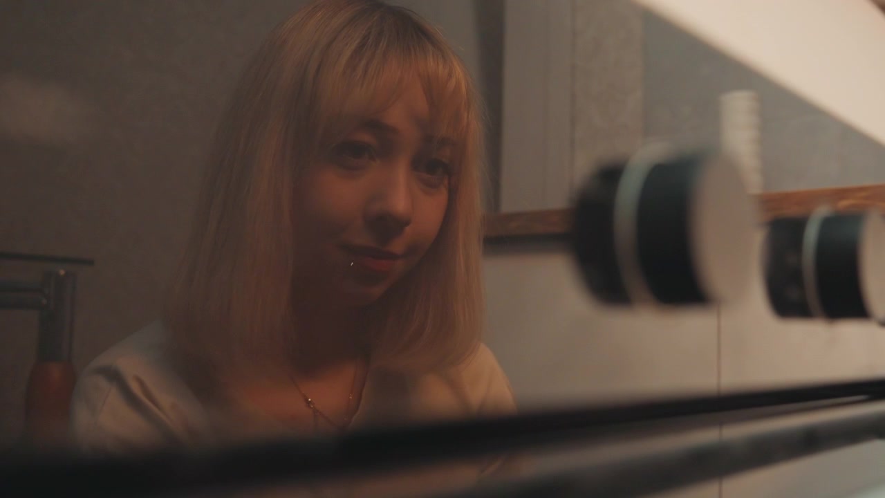 Giovane donna che controlla il riflesso del forno, girando la manopola in una cucina calda e poco illuminata, vetro ravvicinato con grana cinematografica, sorriso sottile e paziente attesa mentre cuoce un piatto fatto in casa, atmosfera domestica accogliente.