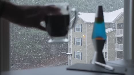 hand picks up glass coffee mug snowing outside apartment building woodstock georgia slow motion