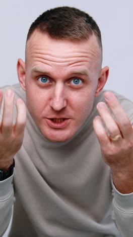 Frowning Caucasian male sitting in the chair. Dark-haired man arguing and gesturing aggressively to camera. Vertical video