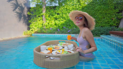 a young woman tourist has her own personal breakfast on a floating table in a private swimming pool
