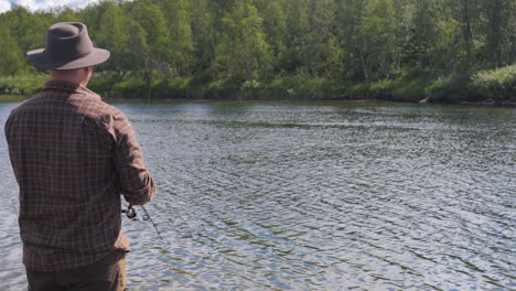 Fisherman-fishing-on-Ume-River-on-sunny-day,-Northern-Sweden