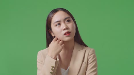 아시아 사업가 여성이 무언가에 대해 생각하고 스튜디오에서 녹색 화면을 둘러보고 있습니다.