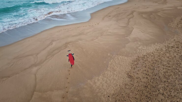 surfer, der auf einem sandstrand spazieren geht und fußabdrücke hinterlässt. schaumiges ozeanwasser