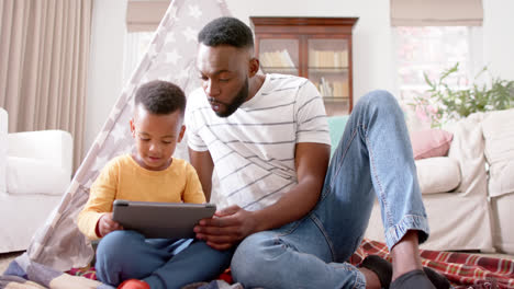 Happy-african-american-father-and-son-using-tablet-and-smiling-at-home,-slow-motion