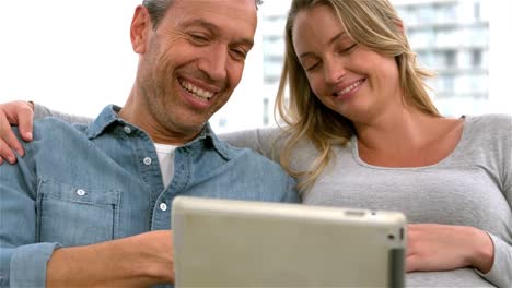 los futuros padres sonrientes usando la tableta