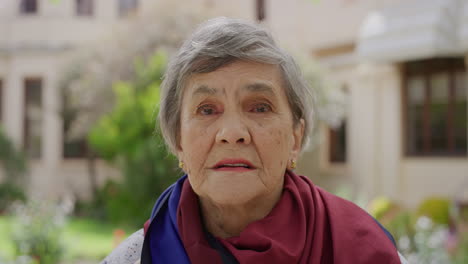 portrait-of-serious-elderly-woman-looking-serious-at-camera-wearing-scarf-in-retirement-home-garden-background