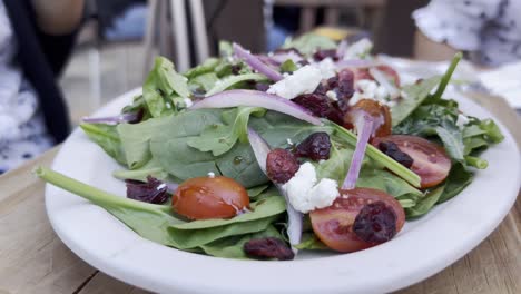 primer plano de un plato blanco con una saludable ensalada de hojas verdes, tomate, pasas, cebolla y roquefort.